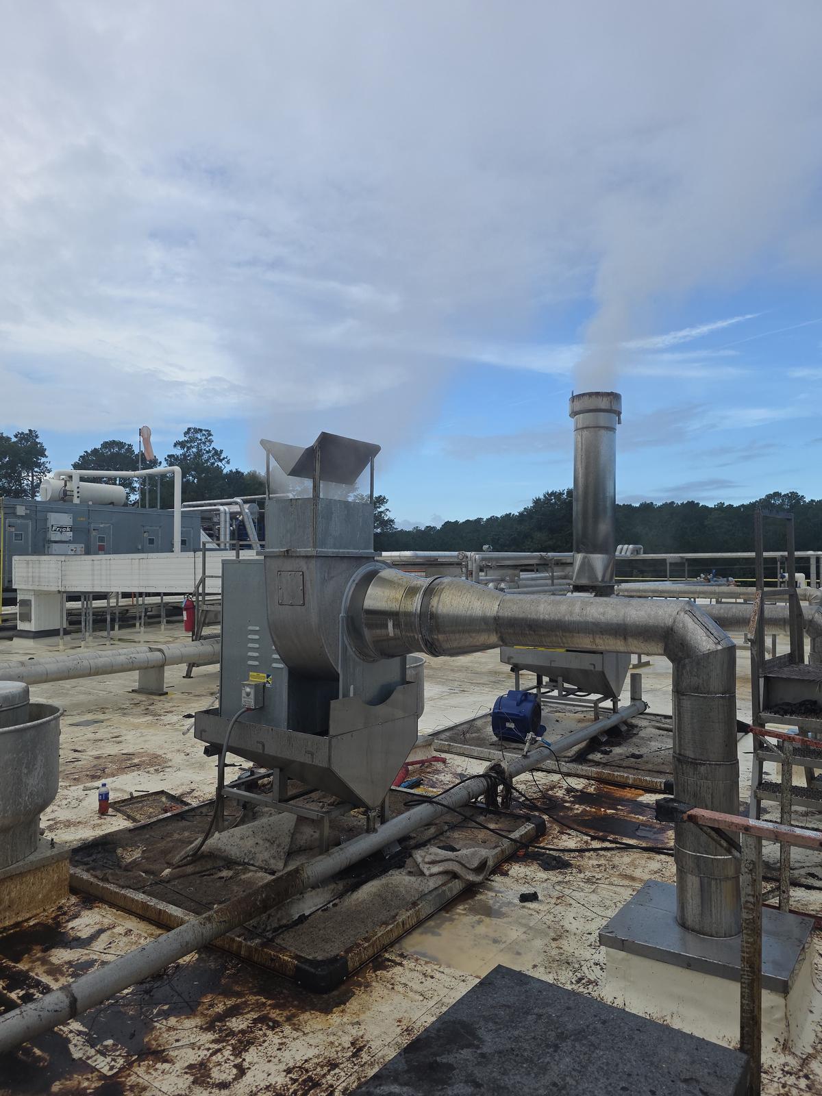 A replacement direct-drive exhaust fan running on the plant roof, discharging a visible plume through its integrated rain cap.